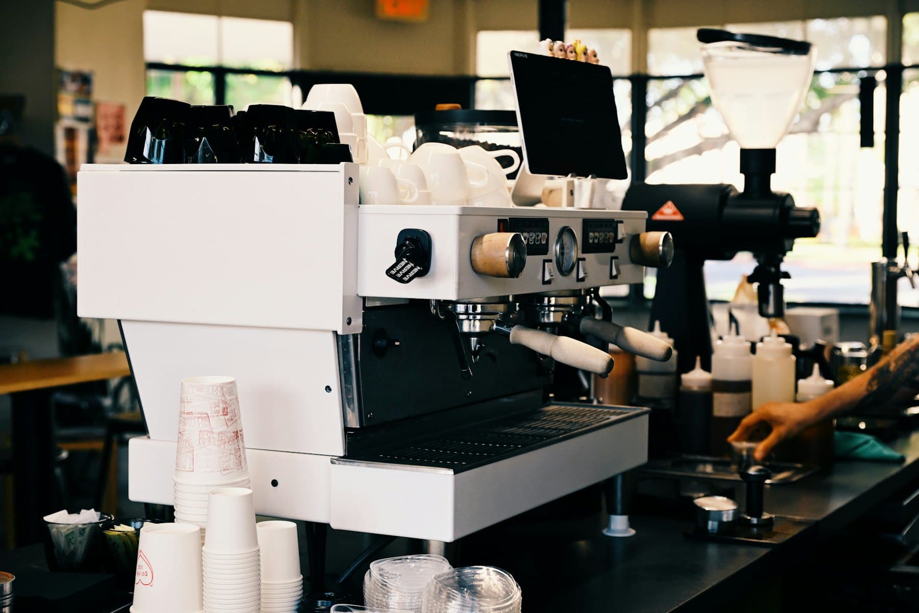 Máquina de espresso blanca en la barra de un café, con vasos apilados
