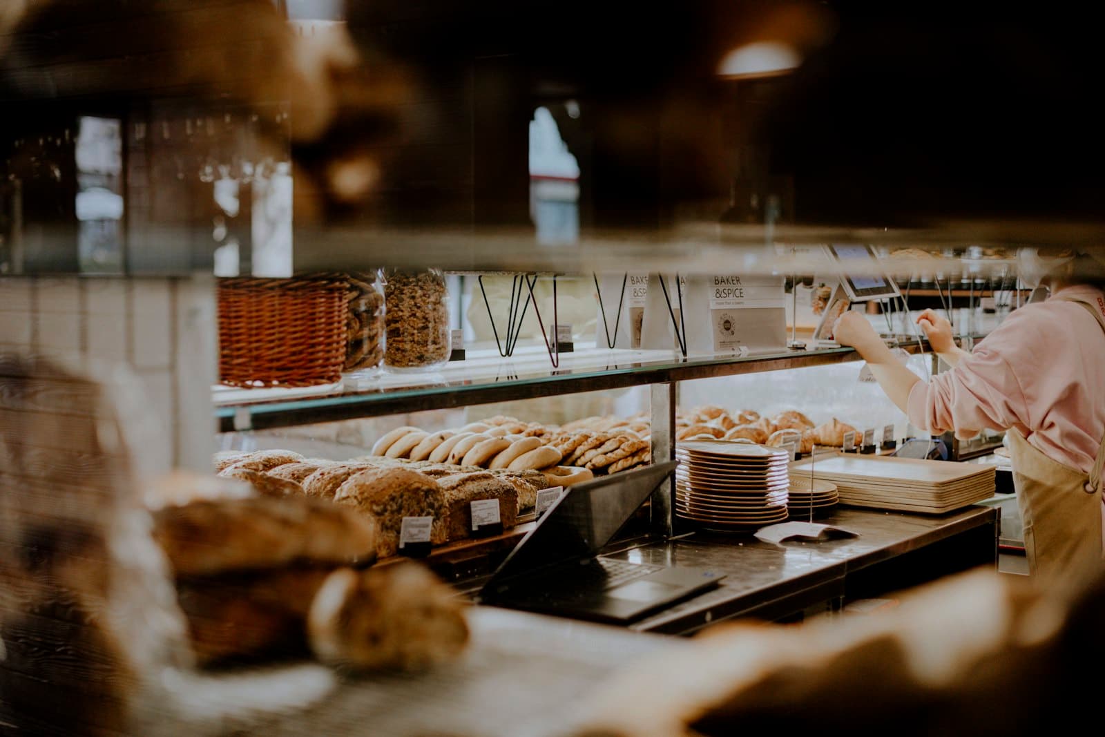 Mostrador de panadería con panes y facturas, y una empleada acomodando bandejas